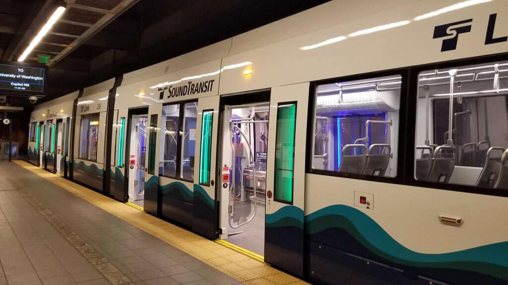 White light rail train car with blue and teal wavey lines painted on the side.