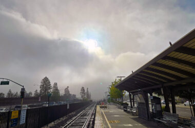 Standing on a train platform with a fog bank breaking with the sun popping out.
