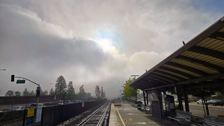 Standing on a train platform with a fog bank breaking with the sun popping out.