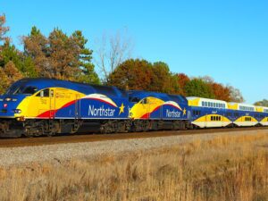 Blue and yellow train travels along autumn colored trees.
