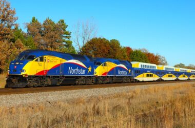 Blue and yellow train travels along autumn colored trees.