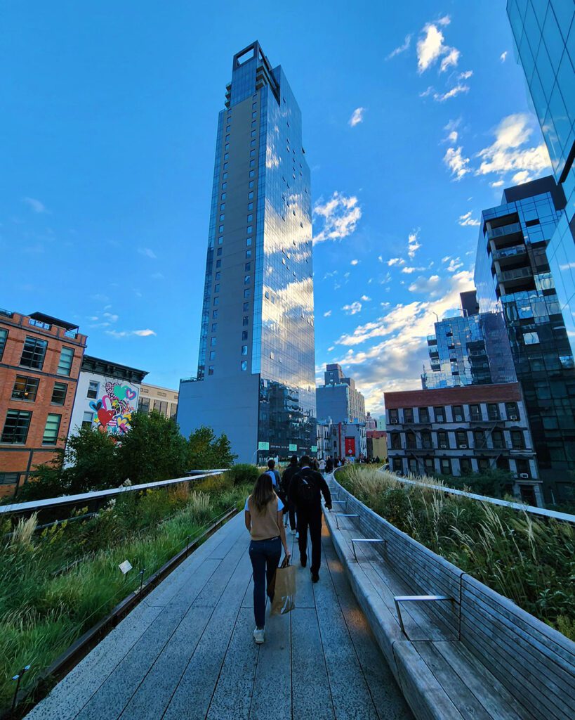 - Vector+Vista People walking on a curved wooden boardwalk in a modern city with glass high-rises and greenery nearby.